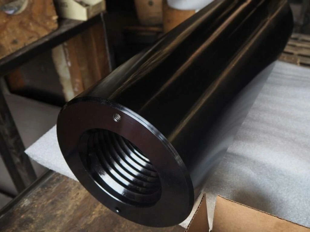 Machined steel cylinder with internal threads featuring a corrosion-resistant black oxide coating.