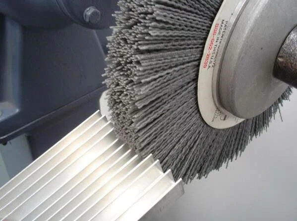 An abrasive wire brush applying a directional brushed surface finish to an aluminum extruded part.
