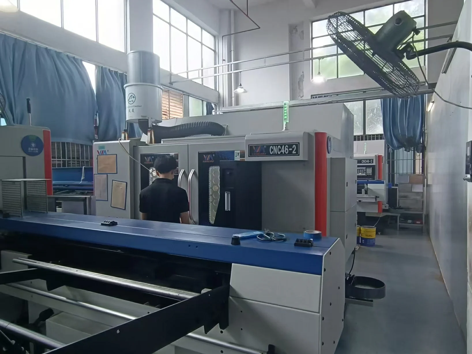 Worker operating automatic CNC turn-mill machine equipped with oil mist collector for precision cylindrical metal parts processing